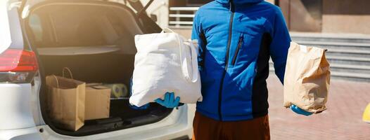 Entrega homem segurando papel saco com Comida perto a carro, Comida Entrega homem dentro protetora mascarar foto