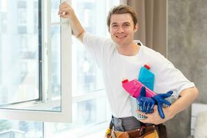 lado Visão do sorridente homem com garrafa do detergente e trapo limpeza janela às casa foto