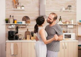 autêntico casal lento dançando durante café da manhã dentro cozinha vestindo pijamas. romântico momento dentro dois, dança e paixão, íntimo feliz brincalhão manhã para jovem marido e esposa, abraçando cada de outros foto