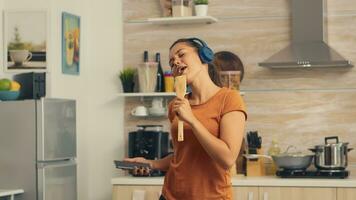 alegre mulher cantando em de madeira colher dentro a manhã ouvindo música em fones de ouvido. enérgico, positivo, feliz, engraçado e fofa dona de casa dançando sozinho dentro a casa. entretenimento e Leise sozinho às casa foto