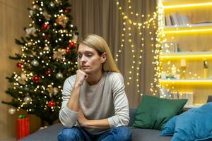 triste mulher sozinho às casa para Natal, sentado em sofá dentro vivo quarto depressivo em Novo ano feriados. foto