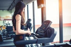 mulher asiática usando telefone inteligente quando treino ou treinamento de força no ginásio de fitness na esteira. relaxe e conceito de tecnologia. exercício esportivo e tema de cuidados de saúde. humor feliz e confortável foto