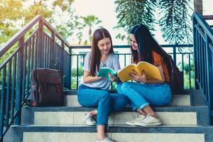 duas garotas de beleza asiáticas lendo e dando aulas particulares para o exame final juntas. estudante sorrindo e sentado na escada. educação e de volta ao conceito de escola. estilo de vida e tema de retrato de pessoas foto