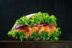 sanduíche com fresco salmão, vermelho cebola e alface dentro uma saboroso Pão Pita, em uma corte borda em uma Sombrio fundo. casa culinária. saudável velozes Comida. foto