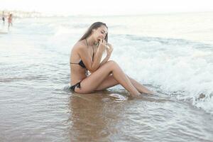 verão período de férias - jovem menina comendo fresco Melancia em arenoso de praia foto