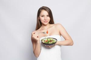 lindo morena menina dentro toalha comendo fresco salada e sorridente foto