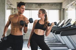 fitness homem e mulher segurando halteres em pé se passando perto da esteira. casal musculoso treinando na academia. foto