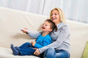 feliz mãe e filho estão sentado em sofá e assistindo televisão junto. foto