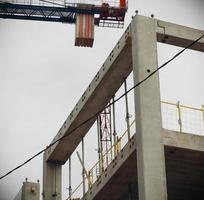 Guindaste de construção sobre carcaça de edifício de concreto no céu branco foto