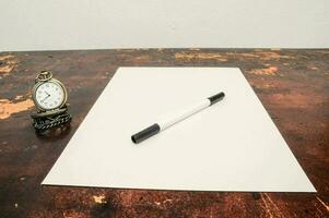 uma branco Folha do papel e uma relógio em uma mesa foto
