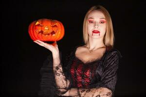 lindo loiro mulher vestido acima gostar a mal vampiro segurando uma abóbora para dia das Bruxas. foto