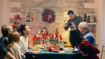 alegre homem levando uma foto do dele lindo família às Natal reunião. tradicional festivo Natal jantar dentro multigeracional família. desfrutando natal refeição festa dentro decorado sala. grande família reunião