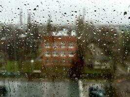 chuvoso dia dentro a industrial cidade. Visão através molhado janela com pingos de chuva momento vendo industrial área durante chuva tempestade. fundo. foto