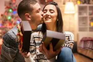 feliz casal se beijando dela namorada bochecha depois de dando dela Natal presente. foto