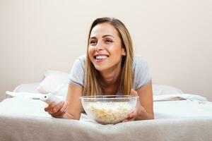 feliz mulher assistindo televisão e comendo Pipoca dentro cama foto