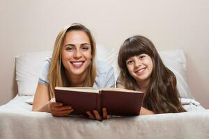 mãe e filha lendo juntos livro na cama foto