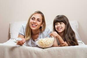 mãe e filha assistindo televisão dentro cama foto