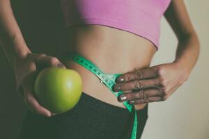 em forma mulher medindo dela fino cintura com uma fita a medida e segurando maçã.focus em estômago. foto