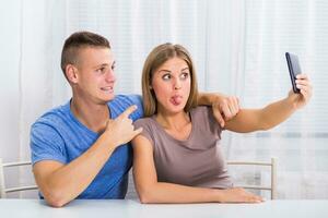 jovem feliz casal sentado às a mesa e levando selfie. foto