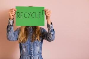 mulher em pé dentro frente do parede e segurando verde papel com palavra reciclar. foto