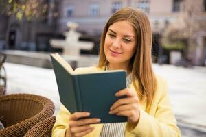 lindo jovem mulher goza lendo livro às a cafeteria. foto