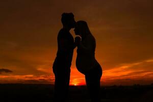 silhuetas do marido se beijando dele grávida esposa para dentro testa e apreciar gastos Tempo juntos ao ar livre.toned imagem. foto