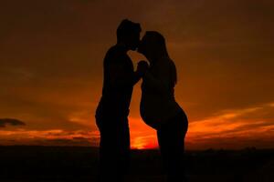 silhuetas do marido e grávida esposa se beijando enquanto elas apreciar gastos Tempo juntos ao ar livre.toned imagem. foto