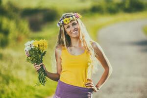 retrato do lindo Loiras mulher com guirlanda segurando flores dentro natureza. foto