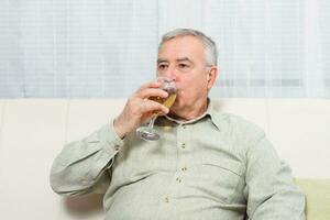 Senior homem goza bebendo vinho às lar. foto