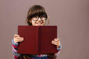 pequeno nerd menina se escondendo atrás uma livro foto