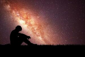conceito de solidão, desespero e arrependimento. homem solitário no prado tendo como pano de fundo as estrelas e a via láctea. foto