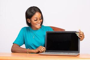 retrato do uma lindo jovem Preto mulher mostrando dela computador portátil tela foto