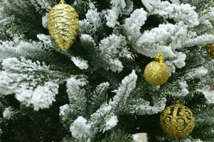 dourado bolas, decorações, brinquedos em a verde galhos do uma fofo coberto de neve Natal árvore. Novo ano feriado fundo. foto