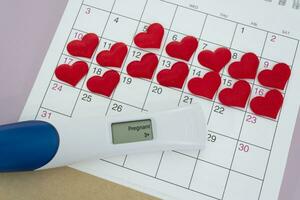 positivo gravidez teste com vermelho coração forma em calendário. foto
