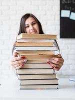 jovem professora sentada com uma pilha de livros olhando para longe, pronta para a aula foto