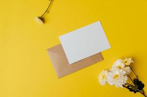 um cartão em branco com envelope e flor é colocado em fundo amarelo foto