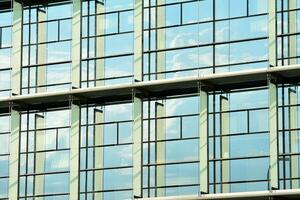 vidro construção com transparente fachada do a construção e azul céu. estrutural vidro parede refletindo azul céu. abstrato moderno arquitetura fragmento. contemporâneo arquitetônico fundo. foto