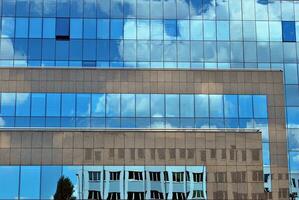 vidro construção com transparente fachada do a construção e azul céu. estrutural vidro parede refletindo azul céu. abstrato moderno arquitetura fragmento. contemporâneo arquitetônico fundo. foto