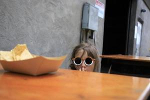 garotinha comendo batatas fritas e salsa em uma mesa foto