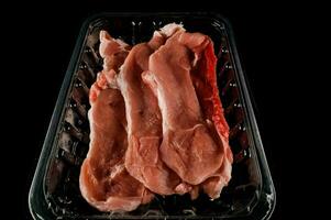 cru carne dentro uma plástico recipiente em uma Preto fundo foto
