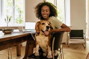 jovem negra acariciando seu cachorro enquanto está sentada à mesa foto