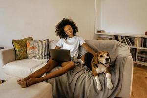 jovem negra usando laptop e acariciando seu cachorro no sofá foto