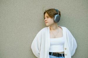 retrato do uma Adolescência menina dentro fones de ouvido contra uma cinzento muro. foto