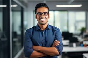 ai gerado uma jovem indiano masculino desenhista, engenheiro, arquiteto quem é vestindo óculos e uma azul camisa sorridente em pé dentro a escritório e olhando às a Câmera foto
