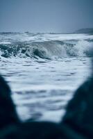 enorme onda às a norte mar com pedras dentro a primeiro plano foto