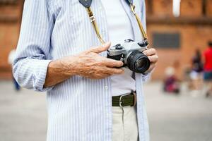 fechar-se e colheita mão do Senior turista segurando dele vintage filme Câmera em borrado do cidade portão fundo. foto