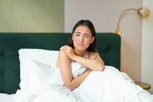 retrato do ásia adolescente menina deitado dentro cama e fazendo careta, relutante para despertar acima, olhando lado de fora janela com franziu a testa, relutante face foto