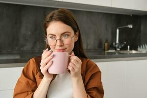 retrato do lindo jovem mulher dentro copos, bebendo café, segurando copo e desfrutando dela chá dentro cozinha foto