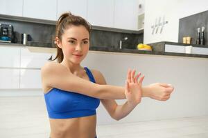 jovem mulher faz exercite-se a partir de lar, senta em ioga esteira e alongar dela mãos, ginástica Treinamento sessão dentro vivo quarto foto