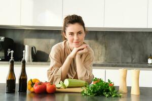 saudável estilo de vida. jovem mulher dentro roupão de banho preparando comida, cortar vegetais, cozinhando jantar em cozinha contador, em pé sobre branco fundo foto